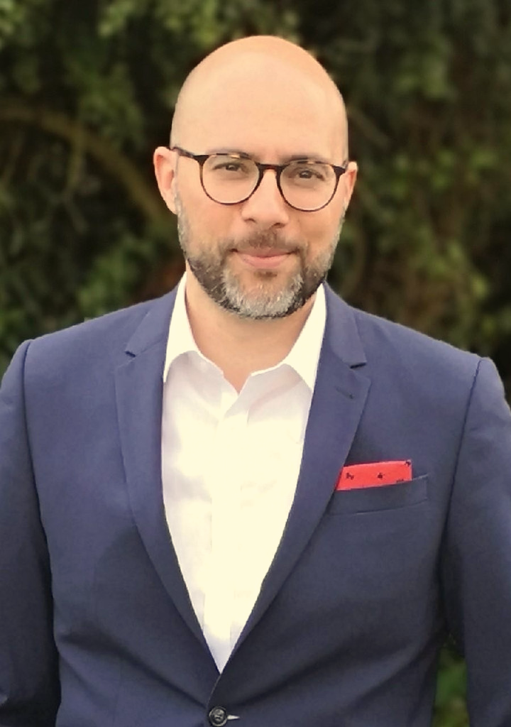 Porträt von Reza Moeini im dunkelblauen Sakko vor grünem Hintergrund